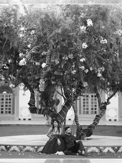 A serene black and white shot of the couple sitting under a large tree, a quiet and timeless moment amidst the wedding festivities.