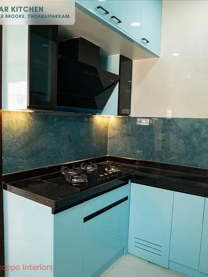 Another view of the light blue kitchen, showing the L-shaped layout and the efficient placement of the hob. The ventilated shutter on the corner cabinet is a small but important detail for specific storage needs.