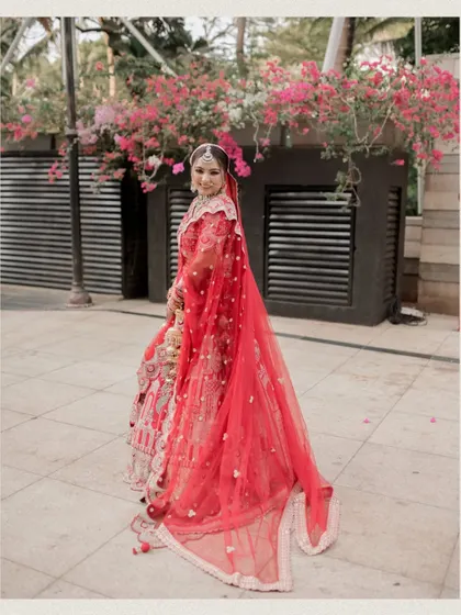 A stunning portrait of the bride in her red lehenga, with a backdrop of pink bougainvillea.