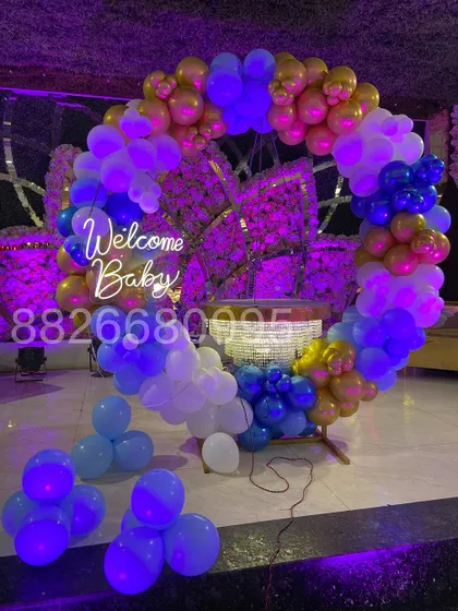 The welcome baby ring backdrop just after setup, showing the vibrant blue, white, and gold balloons and the bright glow of the neon sign.