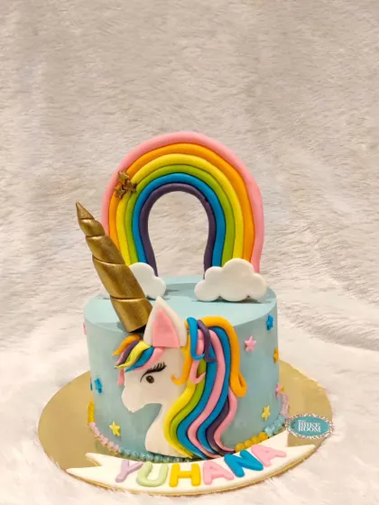 A classic unicorn and rainbow cake. The design features a beautifully sculpted unicorn head with a rainbow mane, a golden horn, and a colorful rainbow arching overhead.