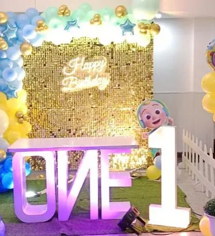A Cocomelon first birthday setup with a gold shimmer wall and a "ONE" table.