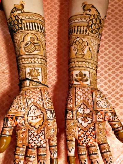 A traditional bridal design with auspicious symbols like the kalash (pot) and swastika. The arms feature peacock motifs, and the entire piece is filled with intricate details.
