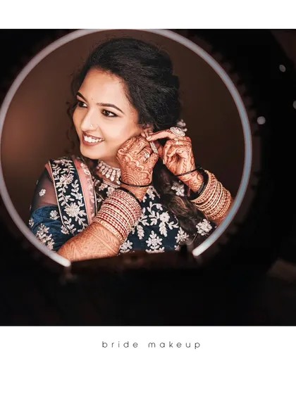 A beautiful getting-ready shot of the bride, her smile captured in the reflection of a ring light as she puts on her jewelry.