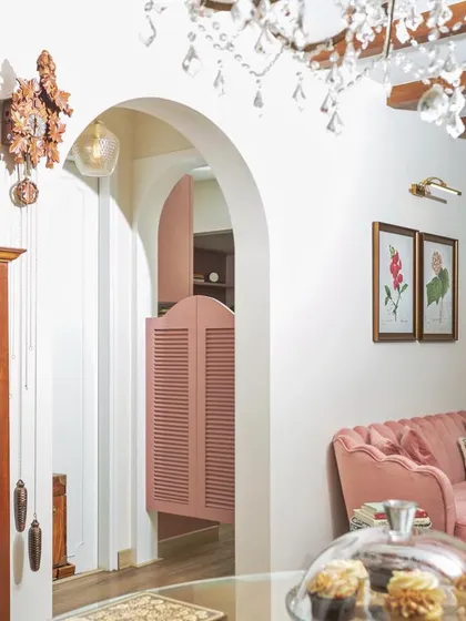 A peek into a space with a charming English cottage feel. The arched doorway, saloon-style pink doors, and classic floral art come together to create a layered, soulful, and wonderfully nostalgic atmosphere.