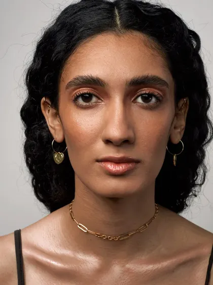 A striking beauty portrait with a focus on glowing skin and minimal jewelry. The warm, peachy makeup tones give the image a fresh and modern feel.