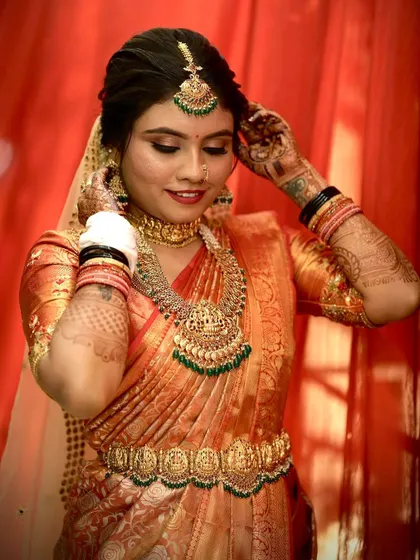 The bride adjusting her earring, showcasing her intricate henna and the flawless finish of her makeup.