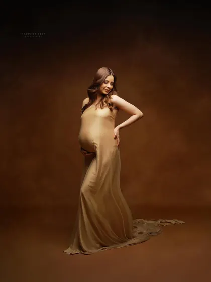 A graceful pose in a sheer golden gown against a painterly brown backdrop. This studio shot focuses on the beautiful curves of pregnancy.