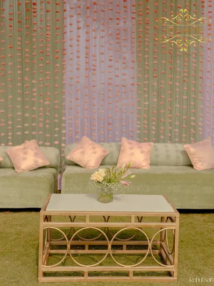 A comfortable lounge area with pastel green sofas, set against a backdrop of hanging sola flower strings.