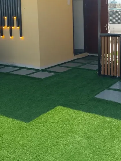 This angle showcases the layout of the terrace, with stone pavers creating a pathway across the artificial turf. The wall-mounted lights add a modern touch and provide ambient lighting.