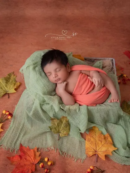 An autumn-themed flat-lay. The simple arrangement of colorful leaves around the sleeping baby creates a beautiful and artistic seasonal portrait.