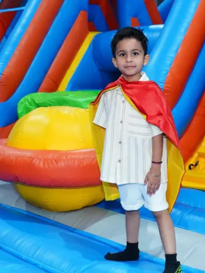 A young superhero surveys his kingdom from the top of an inflatable slide during a themed birthday party.