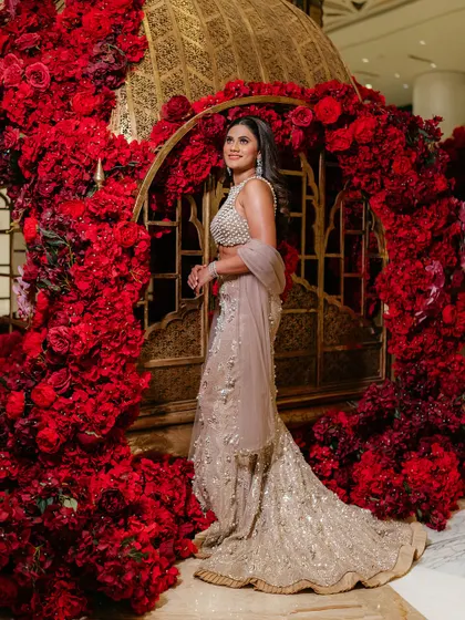 A stunning solo portrait of the bride against a wall of red roses. Her elegant pose and the vibrant background create a breathtaking and romantic image.