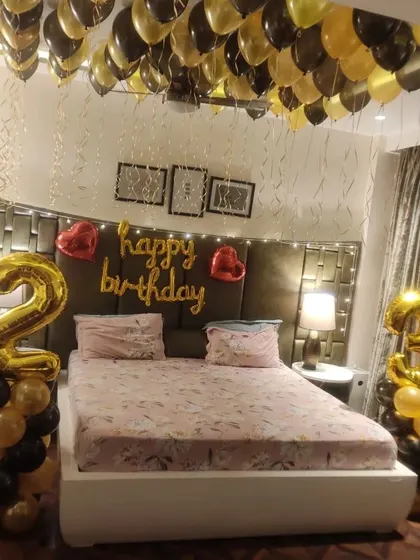 A surprise 28th birthday bedroom decoration. The setup features black and gold balloons floating on the ceiling, large number foil balloons, and a "Happy Birthday" sign above the headboard.