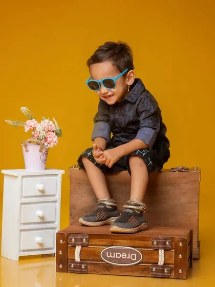 A candid shot of a young boy with a big smile, wearing sunglasses and sitting on a prop box. This photo captures the fun and energy of a kids' studio session.