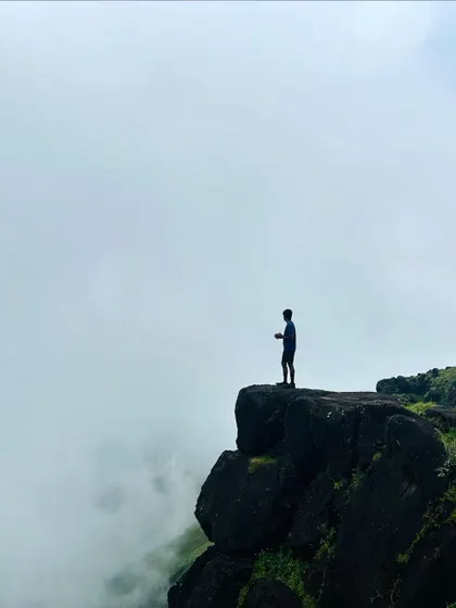 A lone trekker stands silhouetted against the clouds on a cliff at Kumara Parvatha, a truly powerful and inspiring moment.
