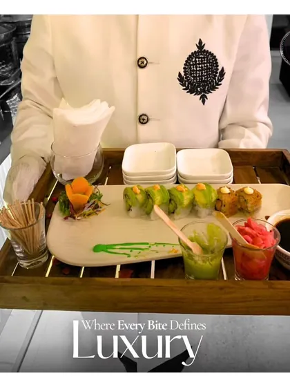 Where every bite defines luxury. A server presents a platter of assorted sushi, beautifully arranged with wasabi and pickled ginger, ready to be enjoyed by guests.