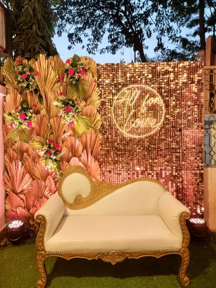 A glamorous photo booth for a Bollywood-themed night. The setup includes a gold sequin wall, a classic diwan, and a neon "All for Love" sign, perfect for capturing star-studded pictures.