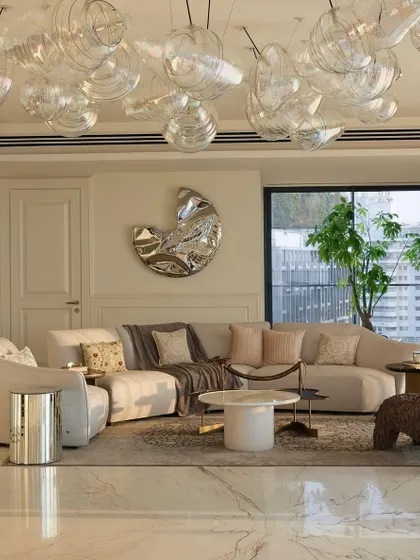 In this 11,000 sq ft South Bombay home, the living room is filled with natural light. We used a massive, cloud-like glass chandelier and a sculptural wall mirror to reflect light and create a sense of airy grandeur. The space opens onto a large deck with city views.