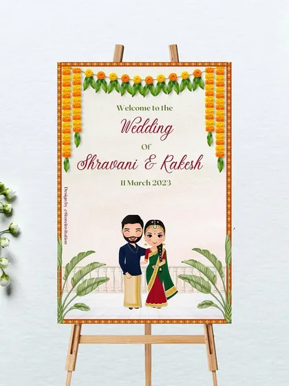 This wedding welcome sign was designed for a South Indian ceremony. It features a traditional marigold toran, banana leaf illustrations, and a custom caricature of the couple in their wedding attire, offering a truly personal touch.