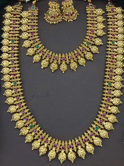 A traditional gold-plated necklace set with red and green stones, ideal for pairing with a silk saree.