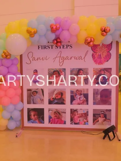 A 'First Steps' milestone board showcasing a year of photos, decorated with a soft pastel balloon arch, celebrating the journey to the first birthday.