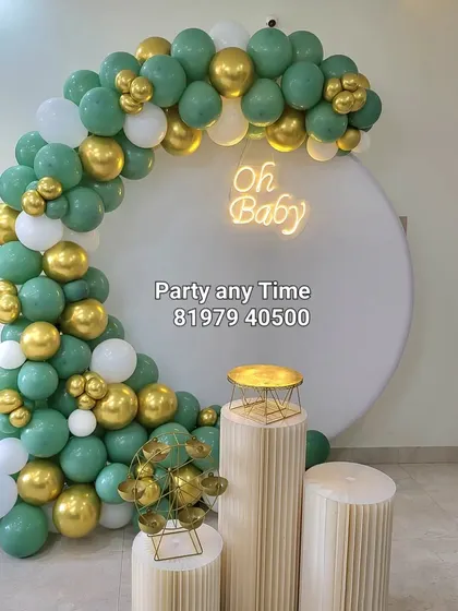 A modern baby shower decoration with a sage green, white, and gold balloon arch.