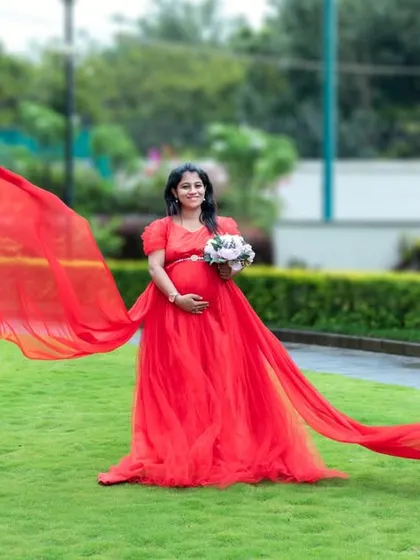 A beautiful shot of a red gown with a long, flying train in a green park.