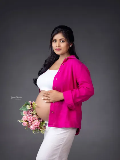 A fresh and modern studio look. Pairing a simple white top and pants with a pop of color from a bright pink shirt creates a casual yet stylish maternity portrait.
