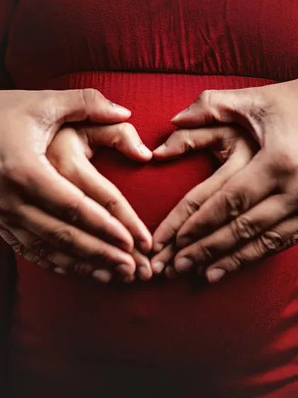 A close-up shot of a couple's hands forming a heart shape on the mother's pregnant belly. This iconic and symbolic image is a powerful representation of love and new life.