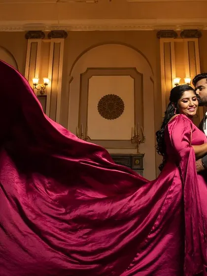 An intimate close-up on a grand staircase, with the groom kissing the bride's forehead, her flowing magenta gown creating a soft, romantic frame.