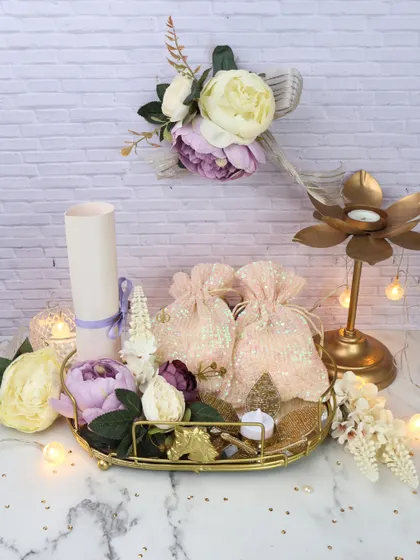 This festive wedding tray is perfect for gifting. It includes decorative potli bags, a scroll, and a lotus-shaped candle holder, all arranged on a golden tray to create a beautiful and traditional present.