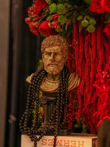 Detail is everything. A classical bust, artfully styled with beads and surrounded by vibrant red florals, adds a touch of artistic flair and sophistication to the decor.