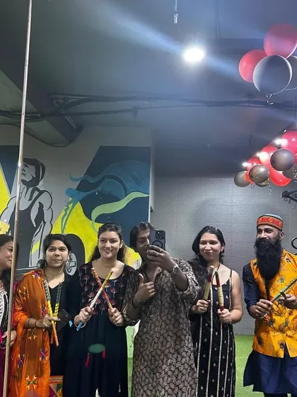 A group of members and trainers posing with their dandiya sticks under the festive decorations.
