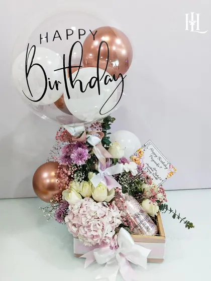 A classic and beautiful birthday hamper designed to delight. It features a mix of pink and white florals, a personalized "Happy Birthday" balloon, and a bottle of sparkling rosé, all presented in a charming pink wooden box.