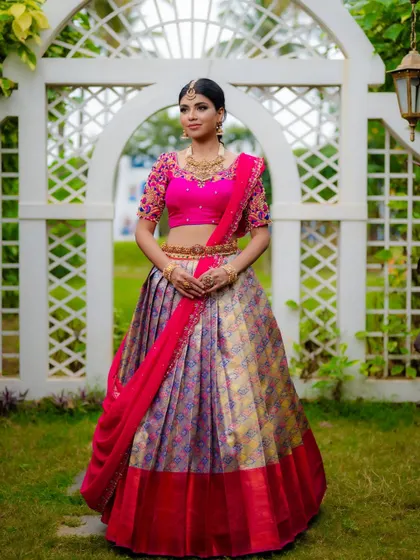 A full-length view of a Kanjeevaram half saree with a multi-colored pleated skirt and a vibrant pink hand-embellished blouse.