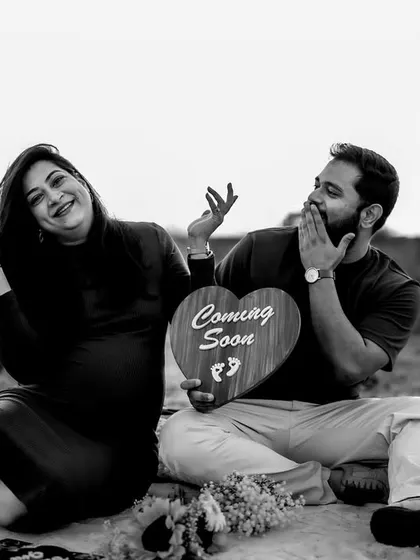 A fun and playful black and white photo of the couple on a picnic blanket, celebrating their "Coming Soon" news with expressive joy.