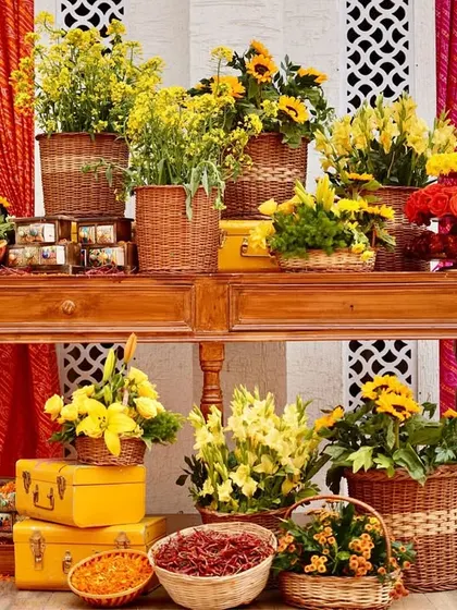 A beautiful display corner featuring a vintage wooden console table laden with baskets of fresh yellow flowers, marigolds, and stacked yellow trunks, creating a rustic and abundant feel.