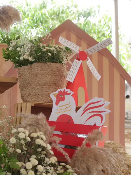 A detail shot of the farm decor, featuring a rooster cutout and a miniature windmill, surrounded by hay and fresh flowers in a woven basket.