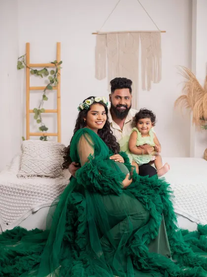 This boho-chic studio setup creates a relaxed and earthy vibe for a family maternity session. The mother's vibrant green gown, the natural textures, and the happy smiles come together for a warm and stylish portrait.