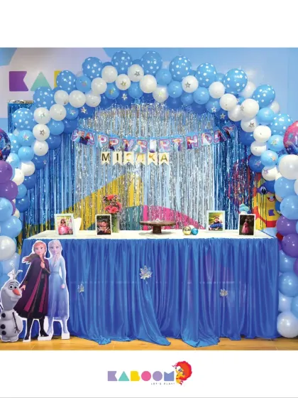 A winter wonderland for a special birthday. This Frozen party setup features a shimmering silver and blue backdrop, character cutouts, and a magnificent balloon arch.
