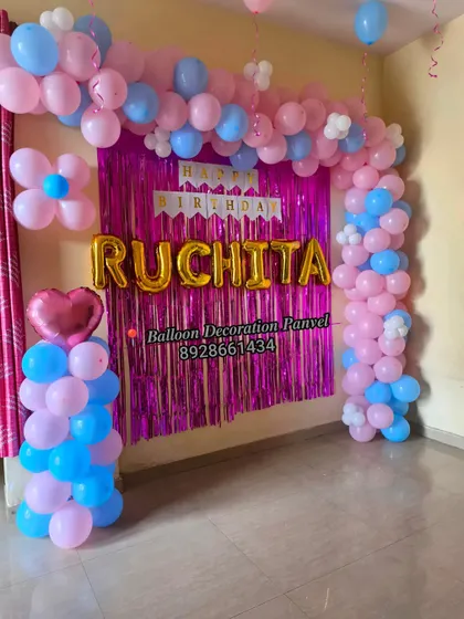 A pink and blue balloon arch decoration for a birthday, featuring a foil curtain and custom name balloons.