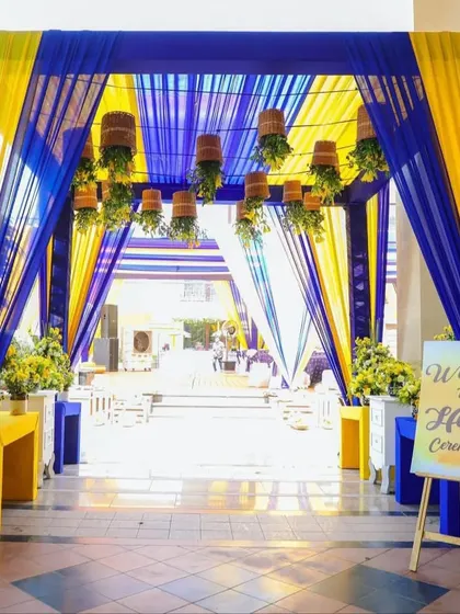 A grand entrance for a Haldi ceremony, draped in bold royal blue and bright yellow fabrics, with hanging potted plants for a unique touch.