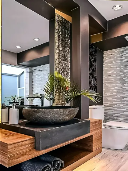 A bathroom design that uses natural and rustic elements for a unique look. The stone vessel sink sits on a wooden vanity, complemented by textured tile walls and warm lighting.