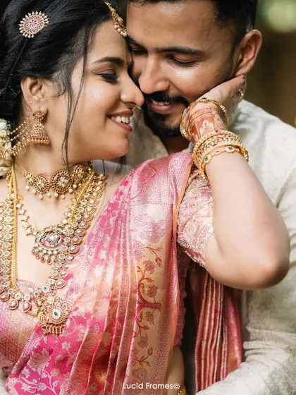 A loving embrace, showcasing the bride's stunning pink saree and temple jewelry.