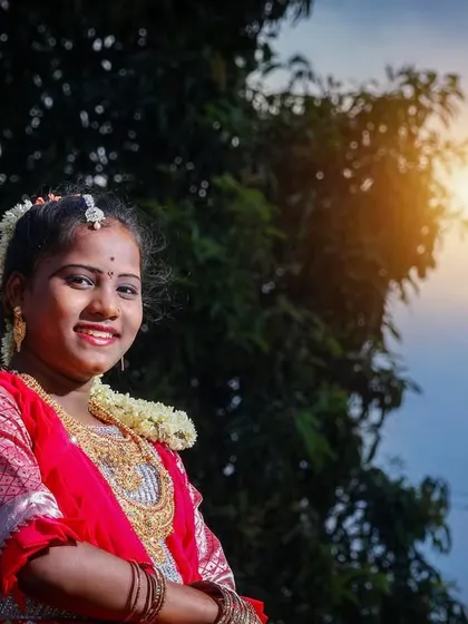 A smiling portrait against a backdrop of trees and sky. The natural lighting is perfect for highlighting the subject's happy expression and the details of her traditional dress.