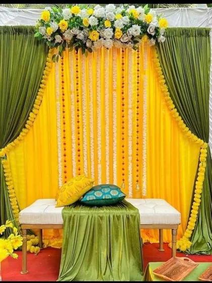 An elegant Haldi setup with a backdrop of yellow and olive green drapes, accented with garlands of white flowers.