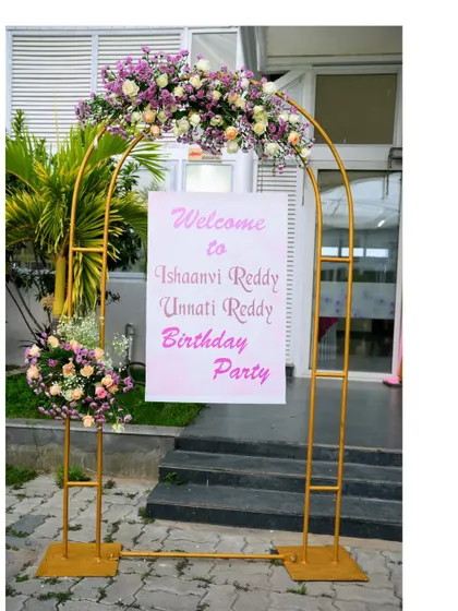 An elegant welcome stand for a twin's birthday party. The golden arch adorned with fresh flowers creates a beautiful and sophisticated entrance for your guests.