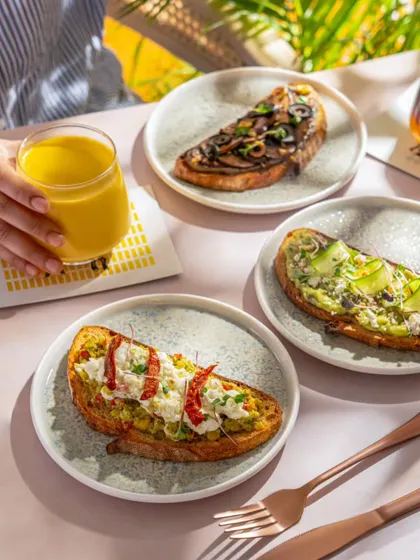 A bright and sunny brunch scene at a Blue Tokai cafe. The image features various toasts and fresh juices, conveying a healthy and delicious start to the day.