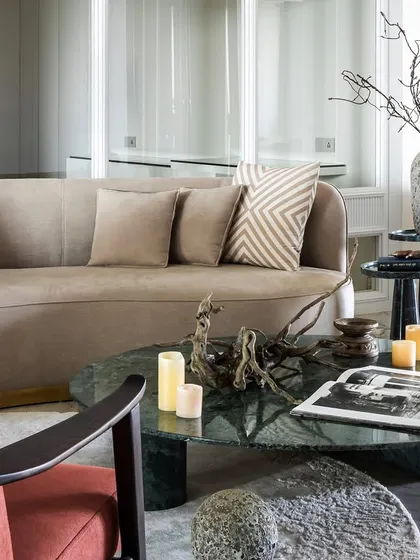 A closer look at the artful arrangement of the living room, with a focus on the green marble coffee table, driftwood sculpture, and the contrast between the red armchair and the neutral sofa.